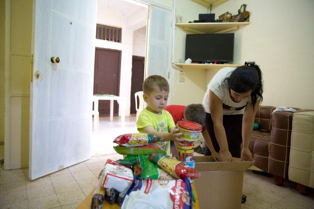 a mother and two sons, one of many families struggling to make ends meet a year after the Beirut port explosion, take groceries out of a food-relief box.