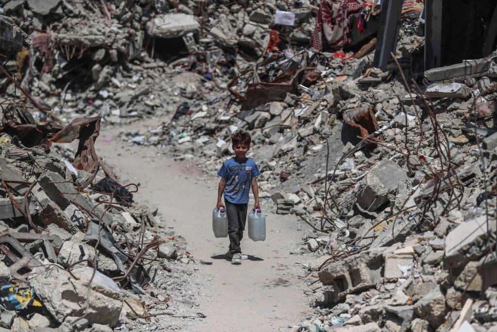 A displaced boy fetches water in a camp in northern Gaza amid the rubble.