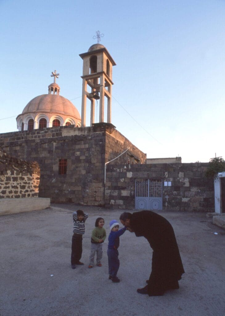 a priest greets three children outside of a church.
