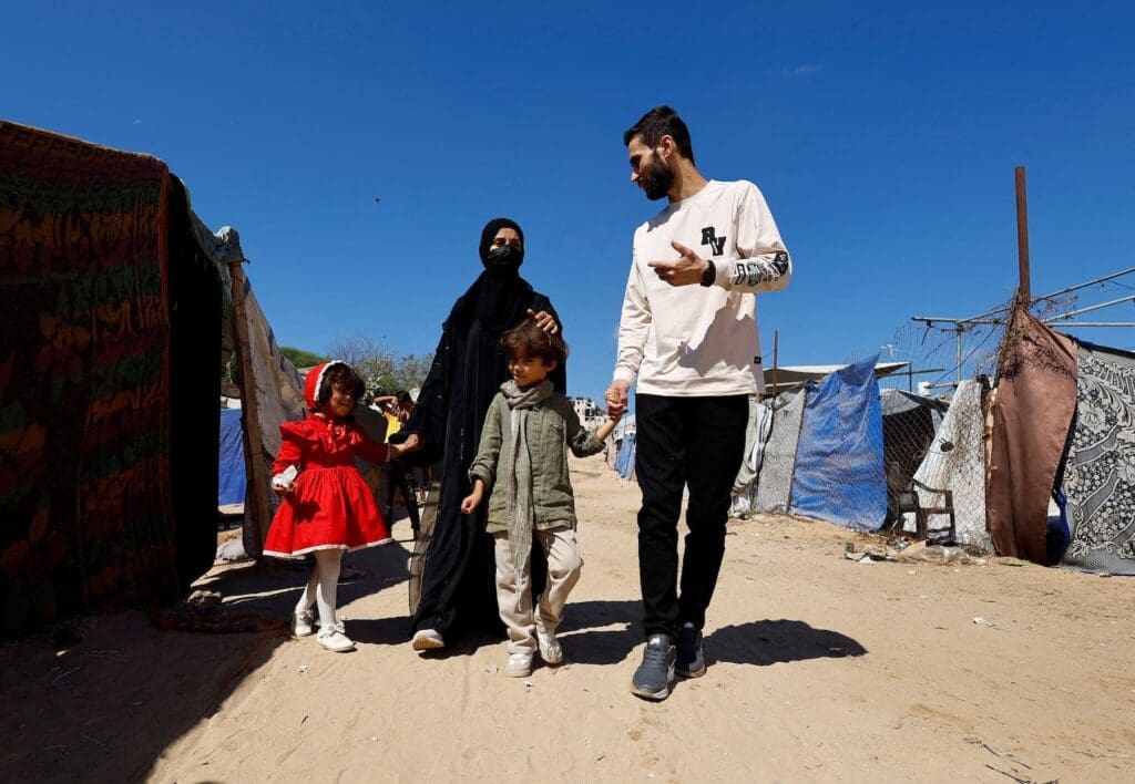 Man, woman and two children walk through tents.