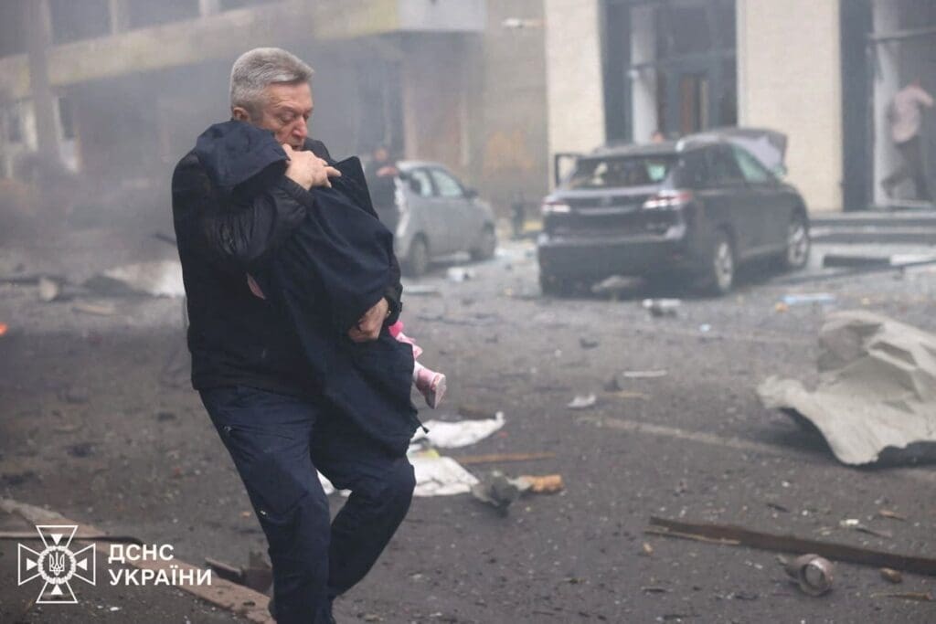 A man evacuates a child from the kindergarten hit by a Russian drone strike.