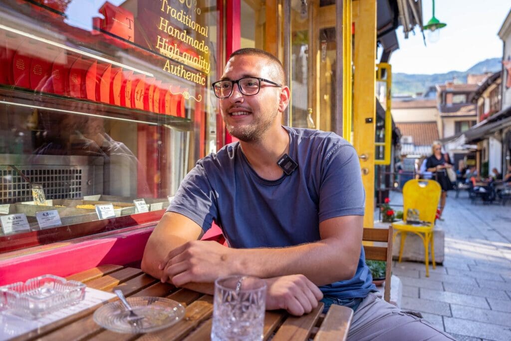 Man waring glasses sits outside a coffee shop.