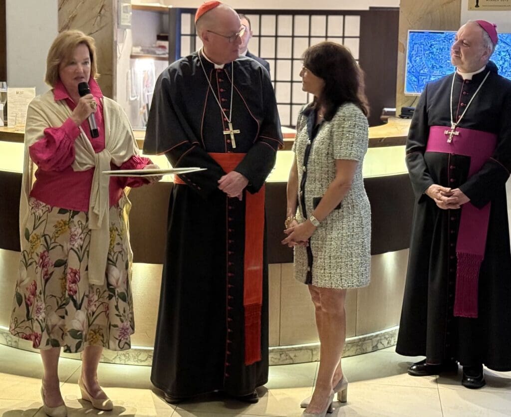Two ladies present an award to Cardinal Dolan while another archbishop observes.