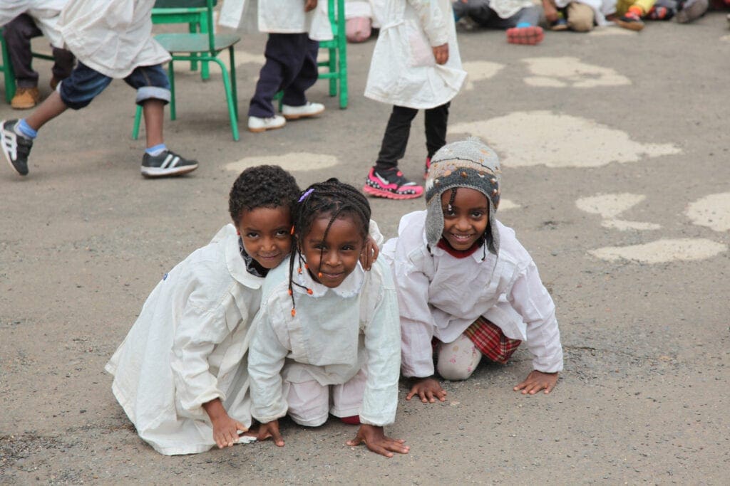 three smiling children in clean white outfits crouch outside in eritrea.