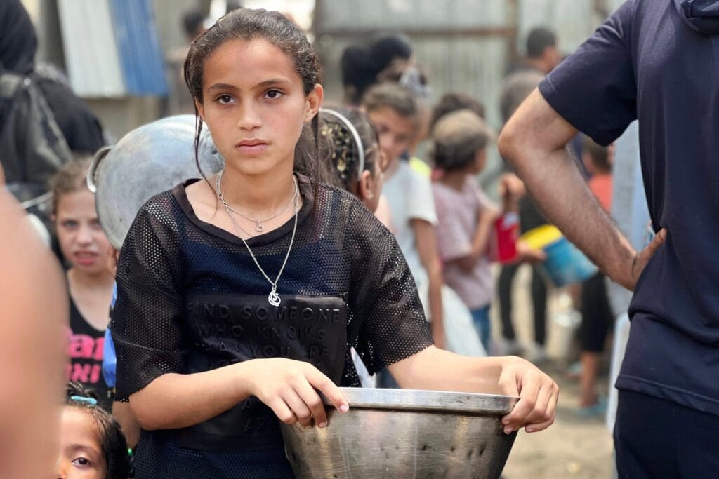 Niña con un recipiente espera en una fila formada por niños.