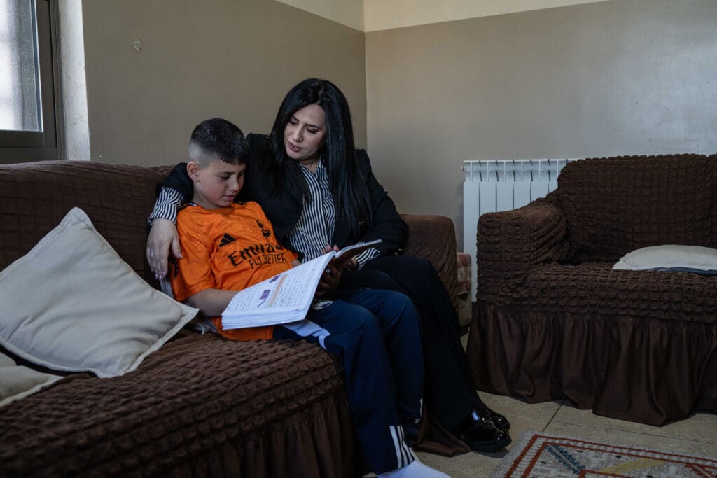Mujer abraza a su hijo en un sofá mientras él lee un libro.