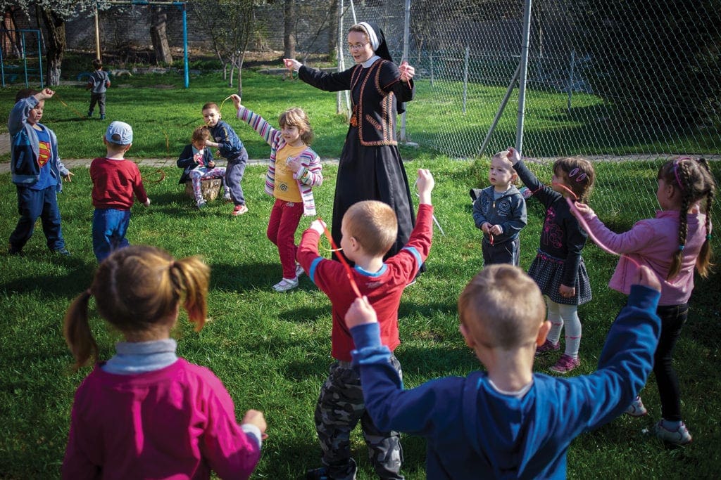 Una monja juega afuera con un grupo de niños.