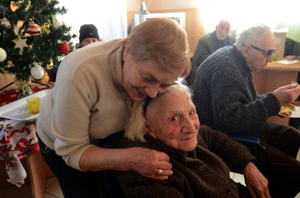 Una mujer abraza a una anciana sentada.