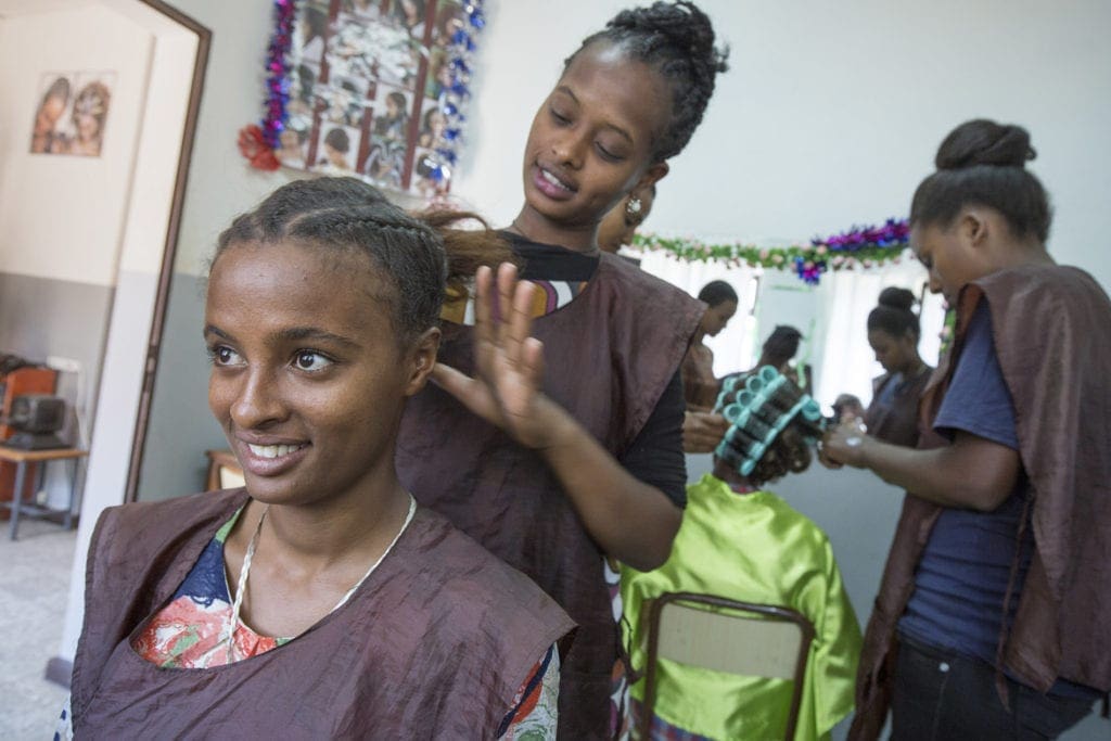 young women practice hairdressing on one another in a small salon.