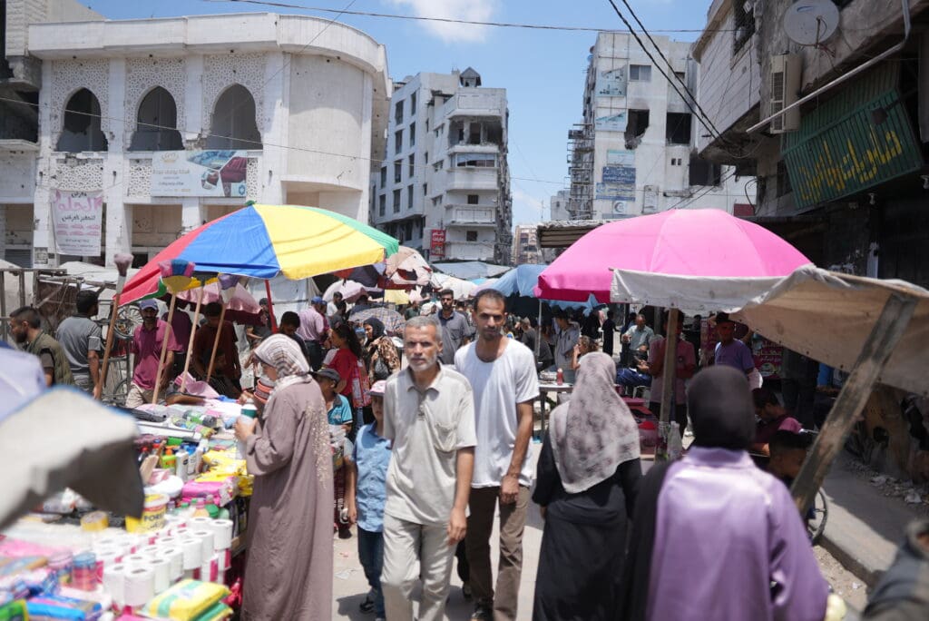 Personas caminan por mercado en la calle en medio de edificios destruidos.