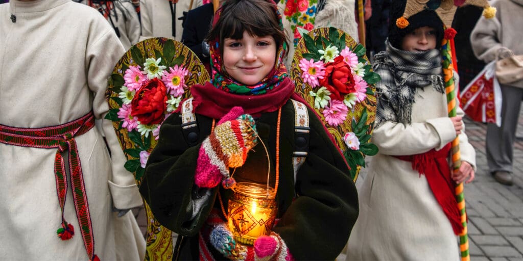 Niña que participa en una procesión, sonría mientras carga una vela.