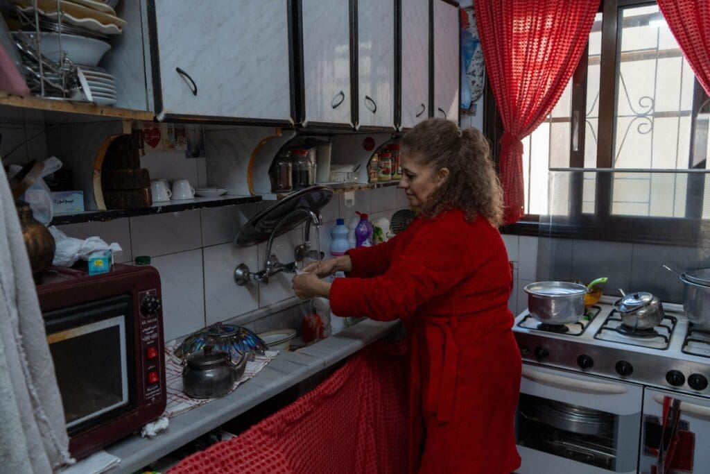 Una mujer vestida de rojo lava un objeto en una cocina.