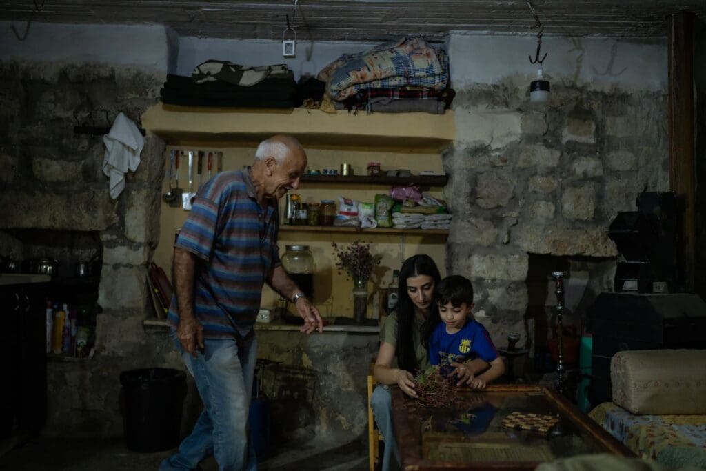 Un hombre mayor sonríe mientras observa a una mujer jugando con su hijo en una mesa.
