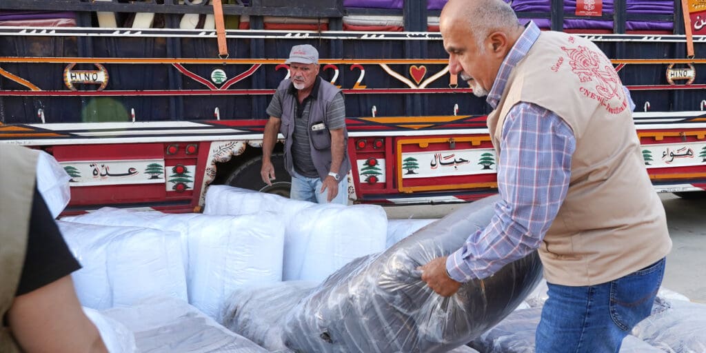 Un hombre que viste un chaleco con el sello pontificio levanta paquetes cerca de un camión.
