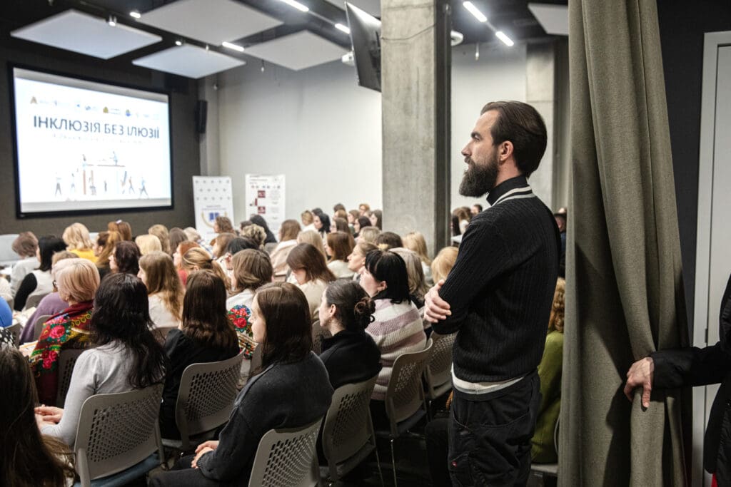 Un hombre de pie mira desde atrás una conferencia.