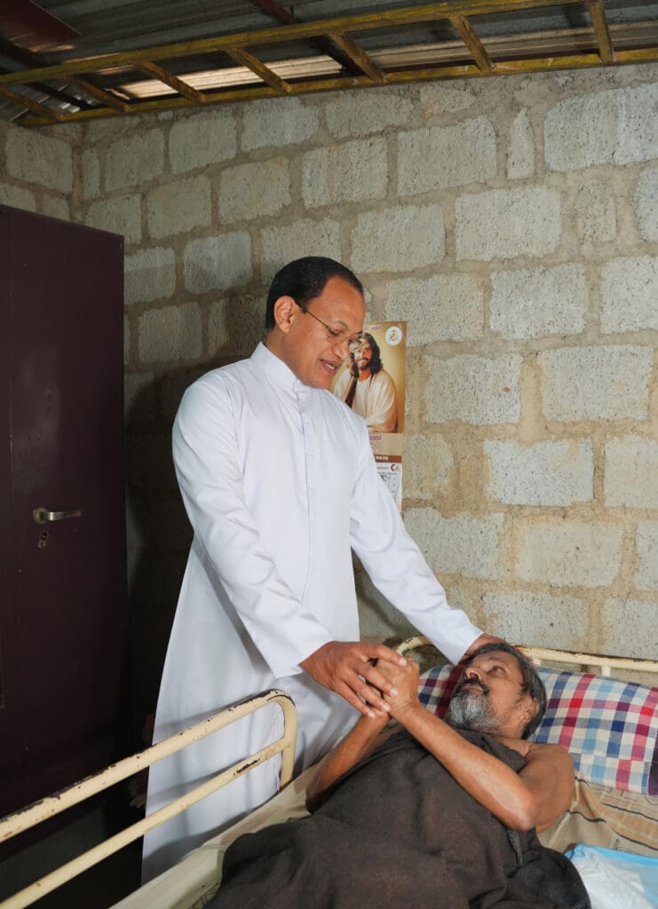 Un sacerdote toma las manos de un hombre en una cama de hospital.