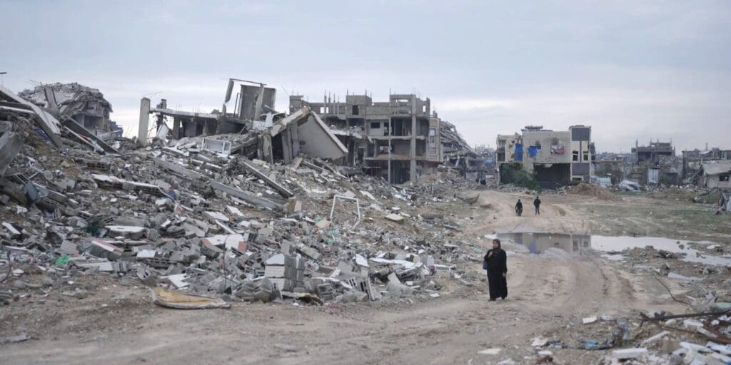 Una mujer en medio de un camino de tierra, rodeada de edificios destruidos.