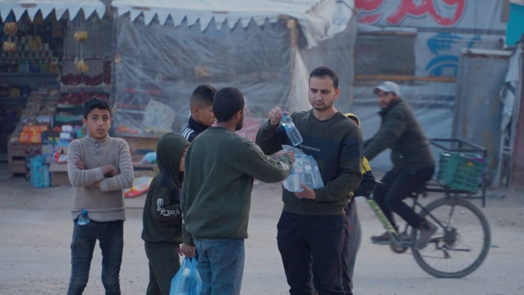 Un hombre reparte botellas de agua en una calle.