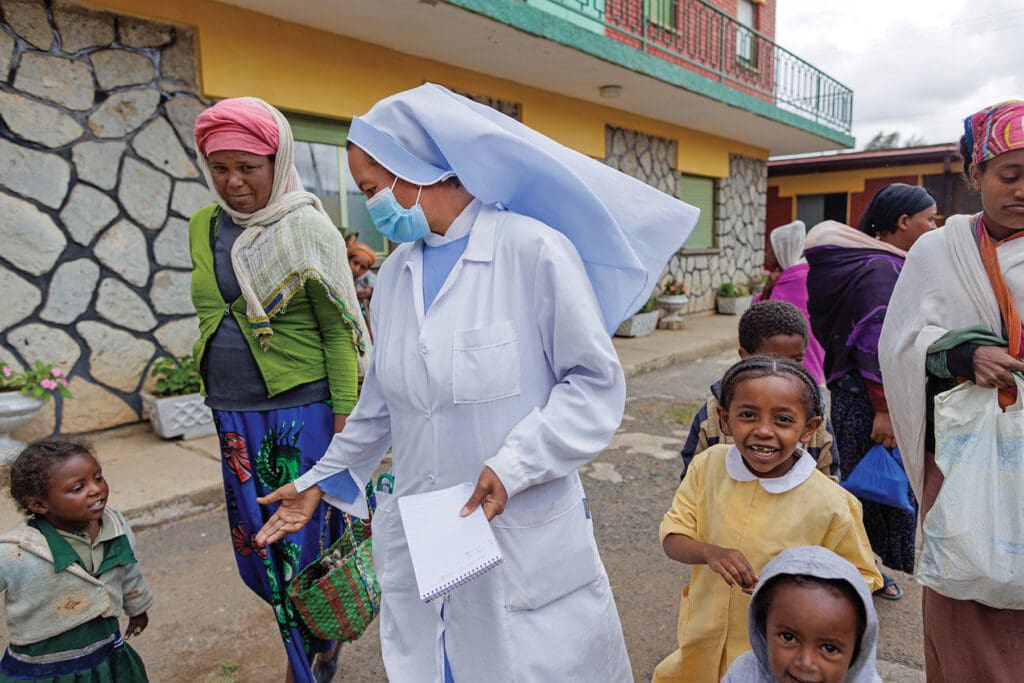 Una religiosa con mascarilla habla con mujeres y niños en la calle.