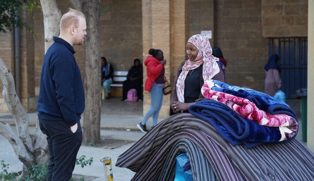 Un hombre habla con una mujer que está de pie junto a un montón de ropa de cama.