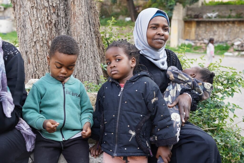 Una mujer africana con tres hijos, uno de ellos un bebé al que carga en brazos.