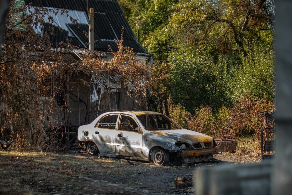 Un auto quemado en medio de una propiedad destruida.