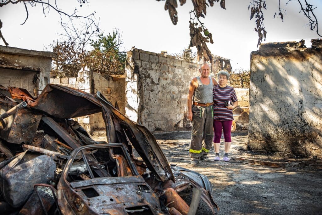 Un hombre y una mujer están abrazados mientras están parados en medio de ruinas.