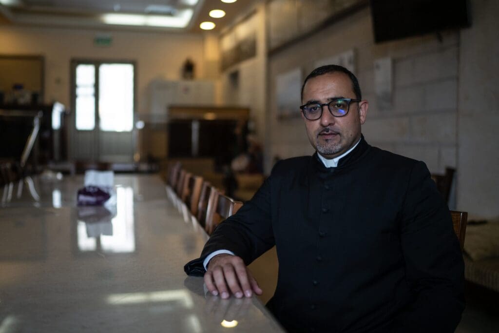 Un sacerdote sentado en una mesa de conferencia.