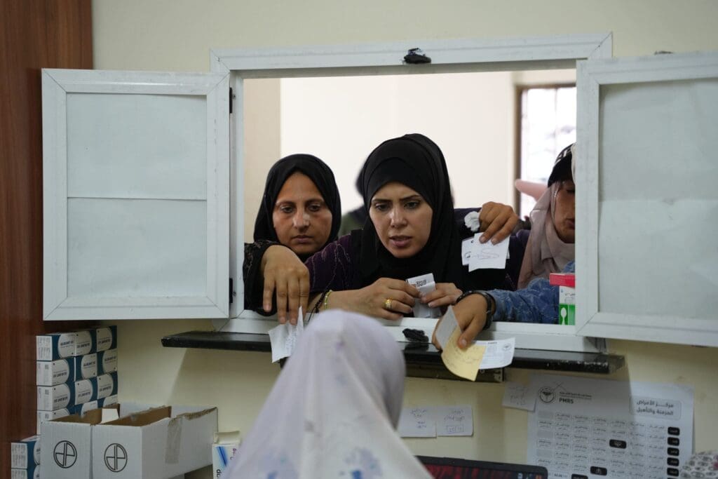 Mujeres abarrotan una pequeña ventana mostrando papeles.