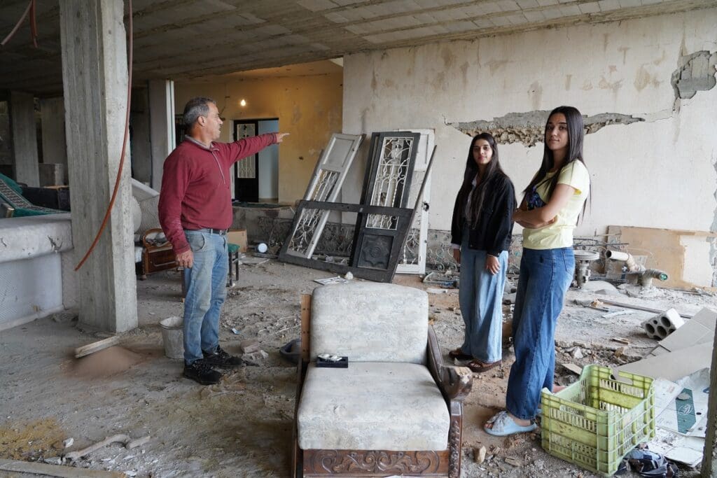 Un hombre y dos niñas observan escombros en una habitación.