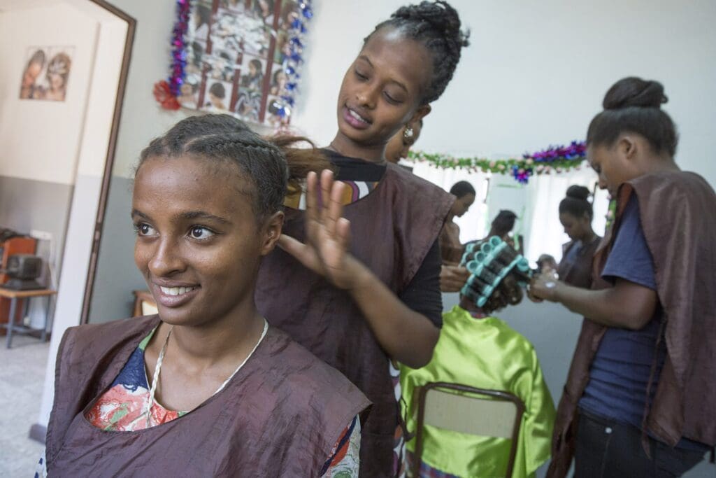 des jeunes femmes s'exercent à la coiffure les unes sur les autres dans un petit salon.
