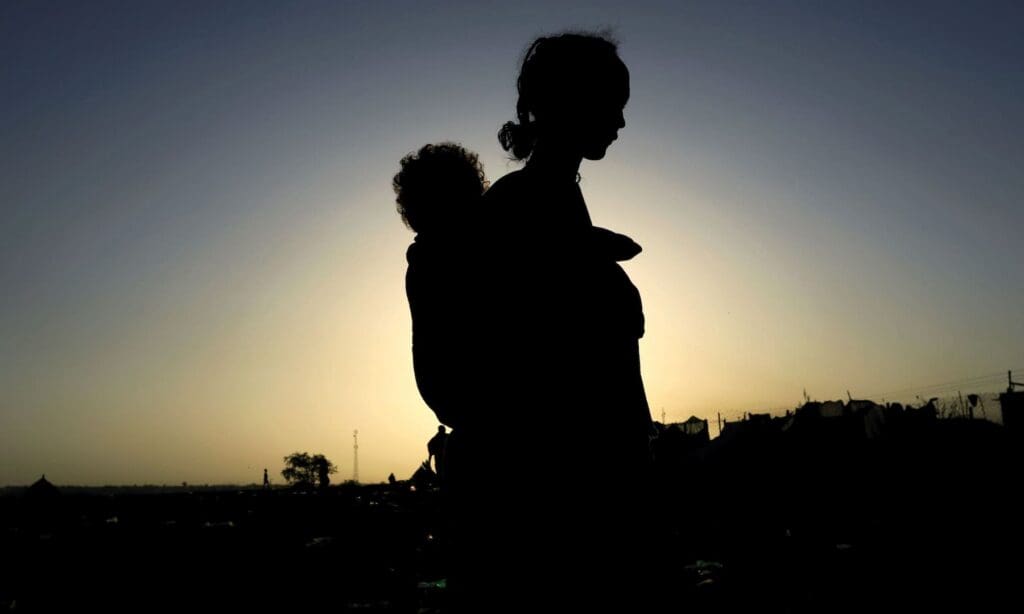 Sagoma di una donna con un bambino sulla schiena contro un cielo blu e giallo.