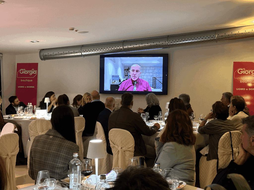 Persone che guardano lo schermo di una TV mentre un uomo parla.
