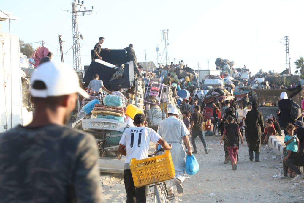 Una strada affollata vicino all’oceano con camion e persone che camminano accanto a loro.