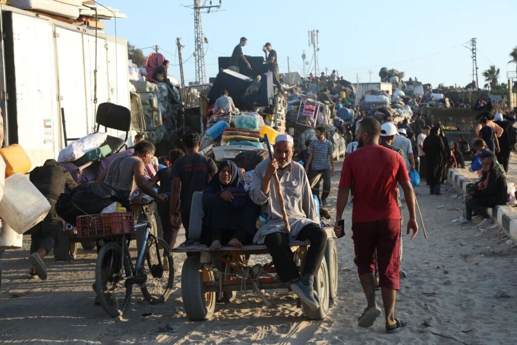 Una folla di persone si dirige lungo una strada polverosa, lasciando il luogo alle loro spalle.