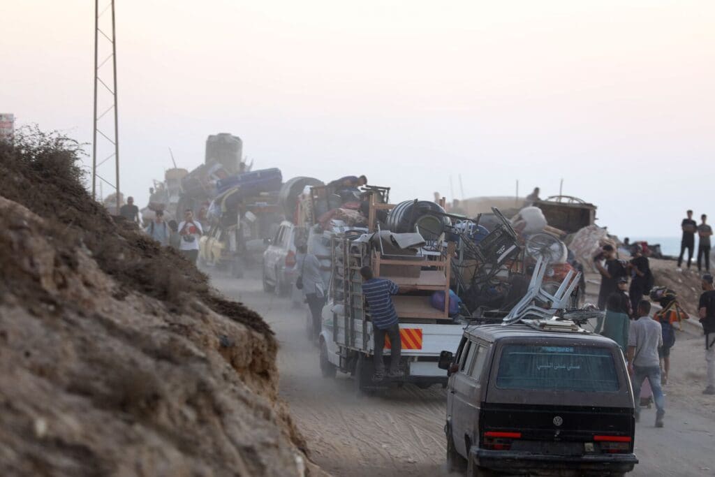 Una folla di persone si dirige lungo una strada polverosa, lasciando il luogo alle loro spalle.