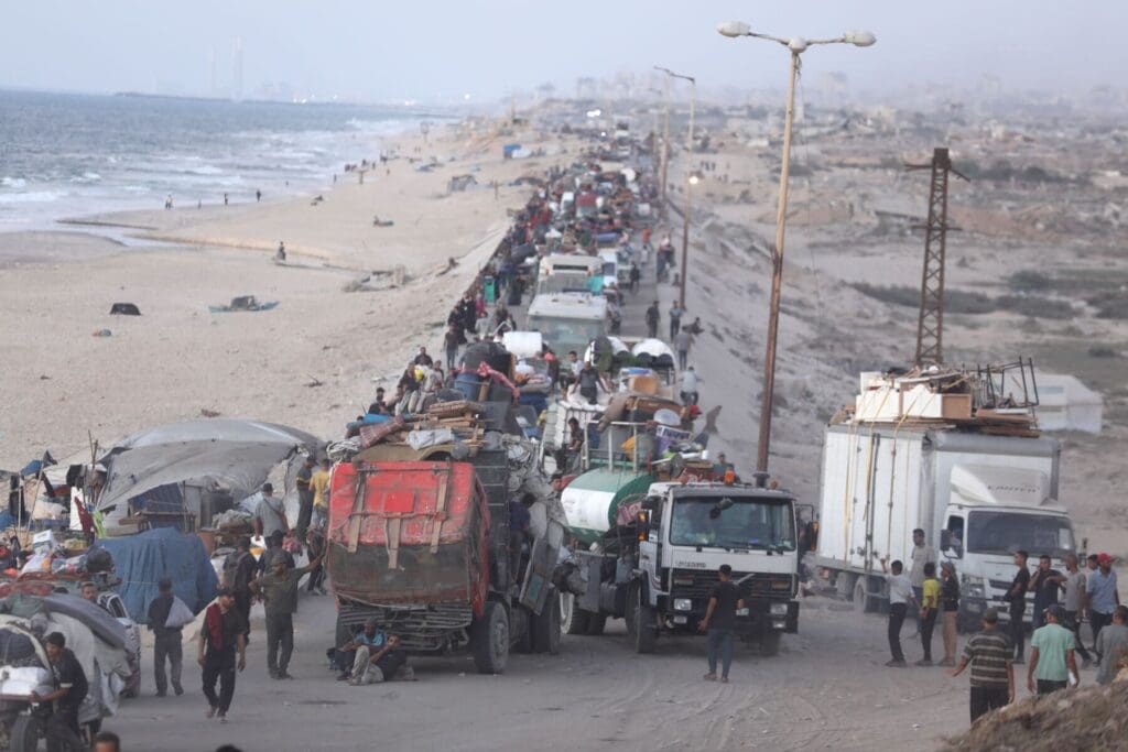 Una strada affollata vicino all’oceano con camion e persone che camminano accanto a loro.