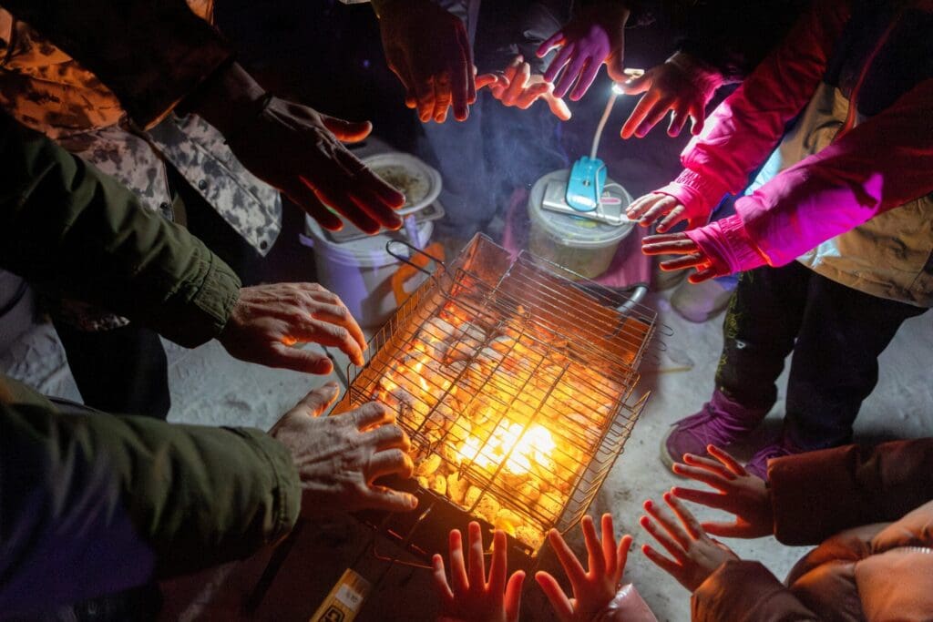 Mani di diverse persone sopra un fuoco acceso.