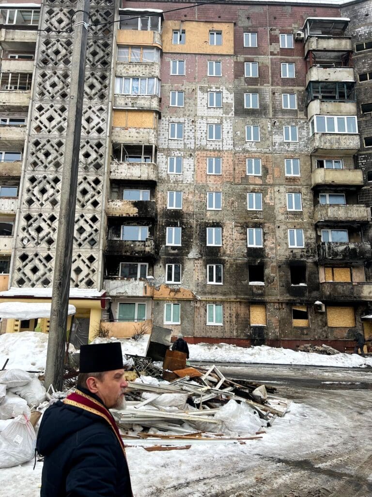 Un sacerdote davanti ad un palazzo quasi distrutto.