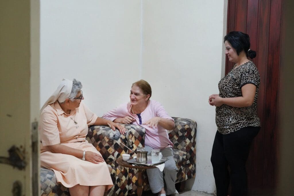 Una religiosa seduta in poltrona parla con due donne.