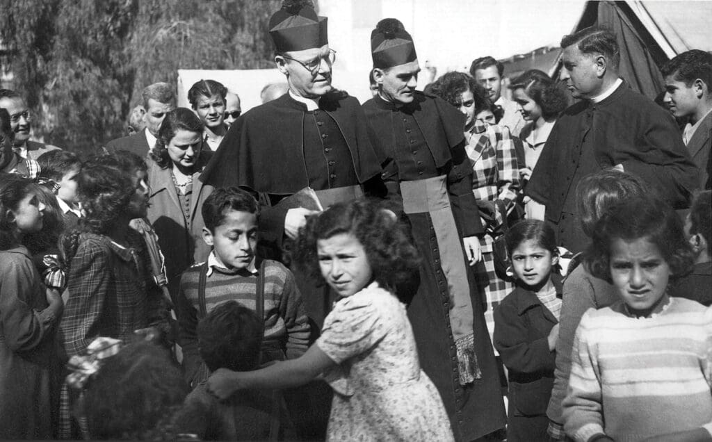 Due sacerdoti camminano circondati da persone e bambini