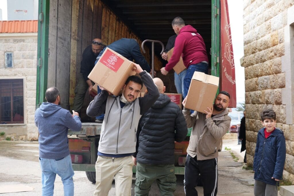 Alcuni uomini sollevano e trasportano scatoloni da un camion parcheggiato lungo una strada.