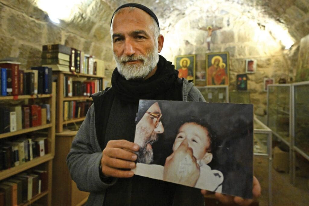 Padre Jihad Youssef tiene in mano un’immagine di padre Paolo Dall’Oglio che sorride con un bambino.