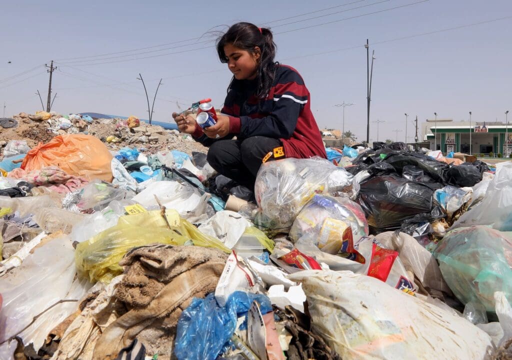 Una ragazza raccoglie lattine da una discarica.
