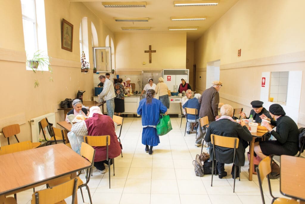 Anziani seduti ai tavoli in un centro comunitario di Tbilisi durante il pranzo.