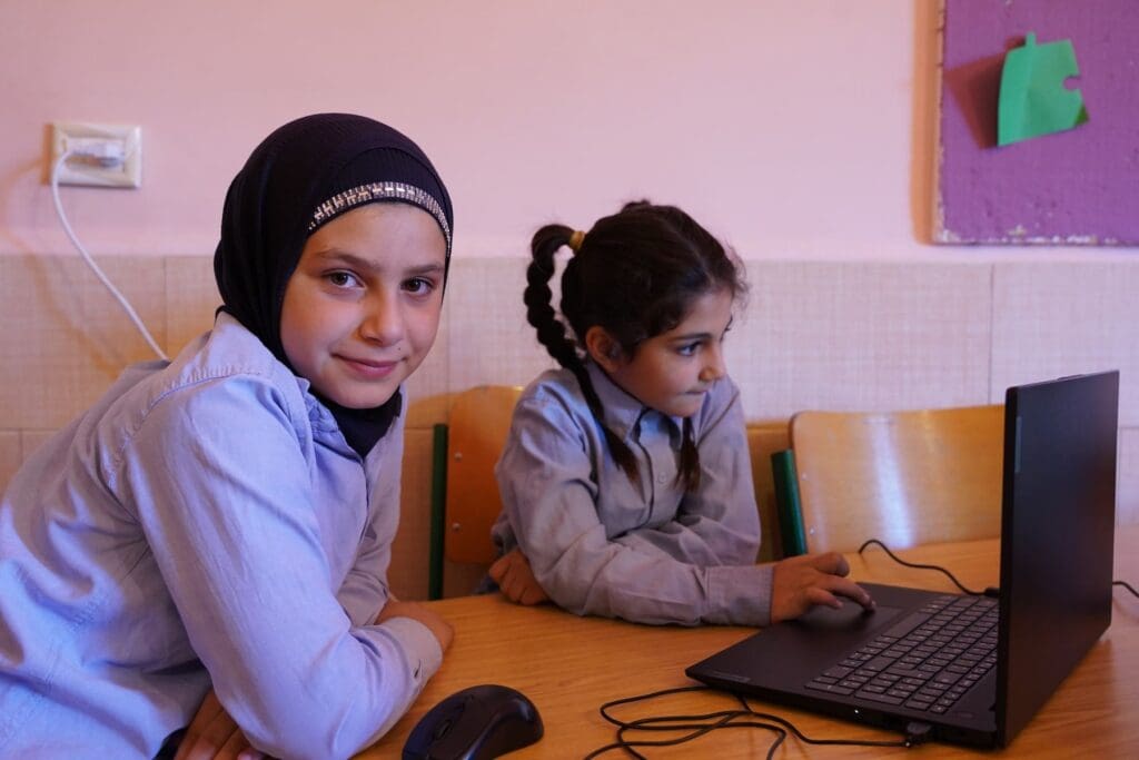 Due ragazze condividono un computer portatile in un’aula scolastica.