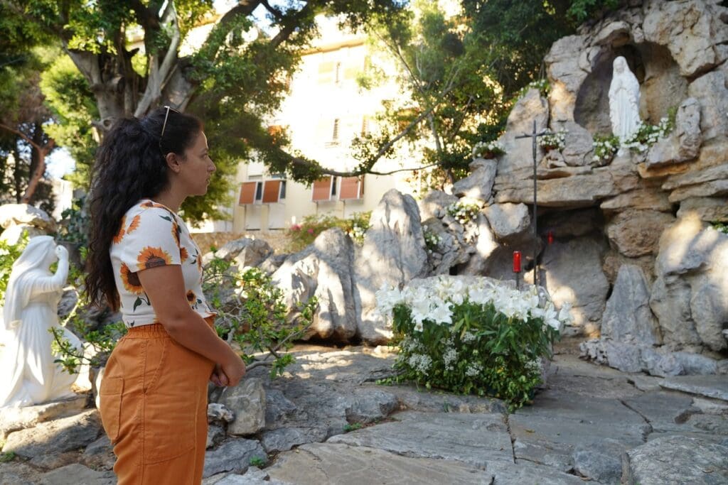 Una donna prega davanti a una statua della Vergine Maria in una grotta votiva.