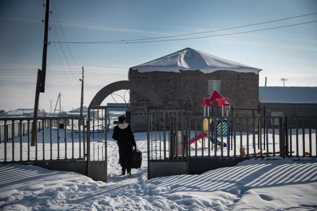 Priest walking through snow on path toward church.