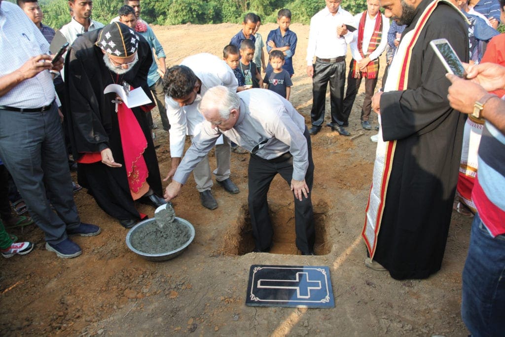 Clergy gathered around a hole in the ground help to lay a cornerstone for a church.