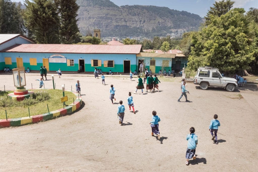 Youth in blue uniforms walk around outside of kidane mehret school buildings.